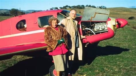 Archival colour photograph of a man and woman standing beside a red aircraft.